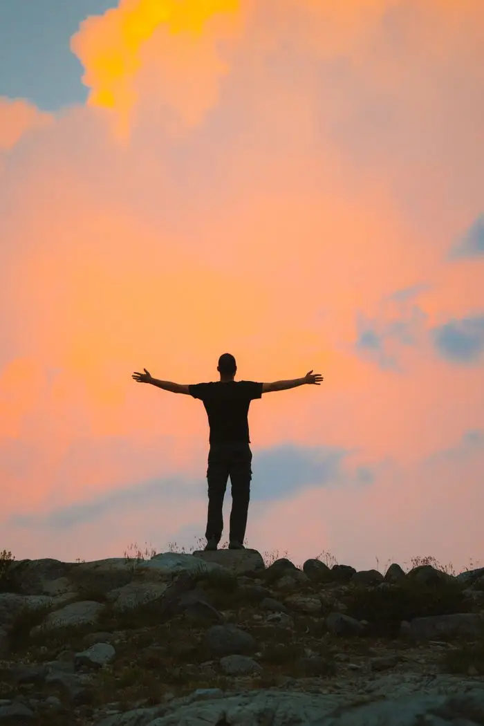 Silhouette of a man with raised arms against a colorful sunset sky, symbolizing freedom and relaxation.